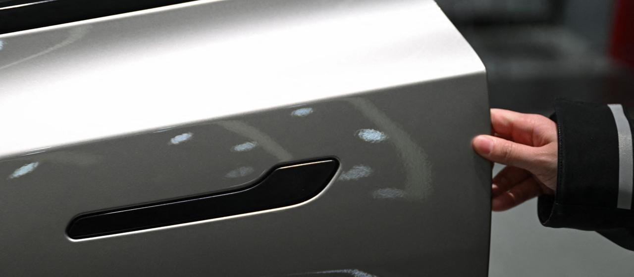 Une femme ouvre la porte d’un véhicule électrique Tesla Model YL dans une salle d’exposition à Pékin.